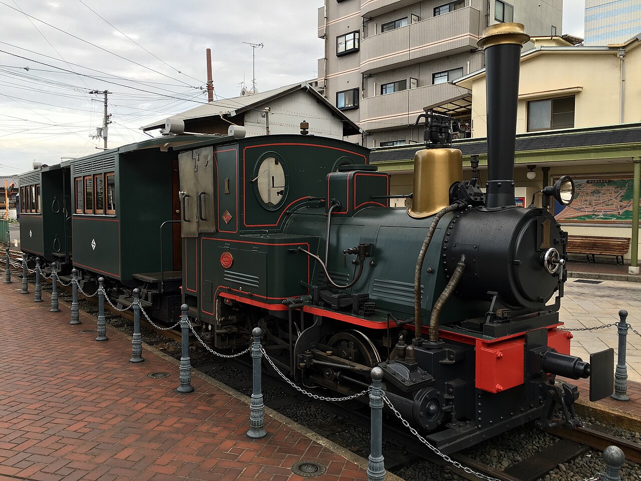 The preserved Botchan Train steam locomotive and carriages parked at Dogo Onsen Station, with the town's buildings in the background.
