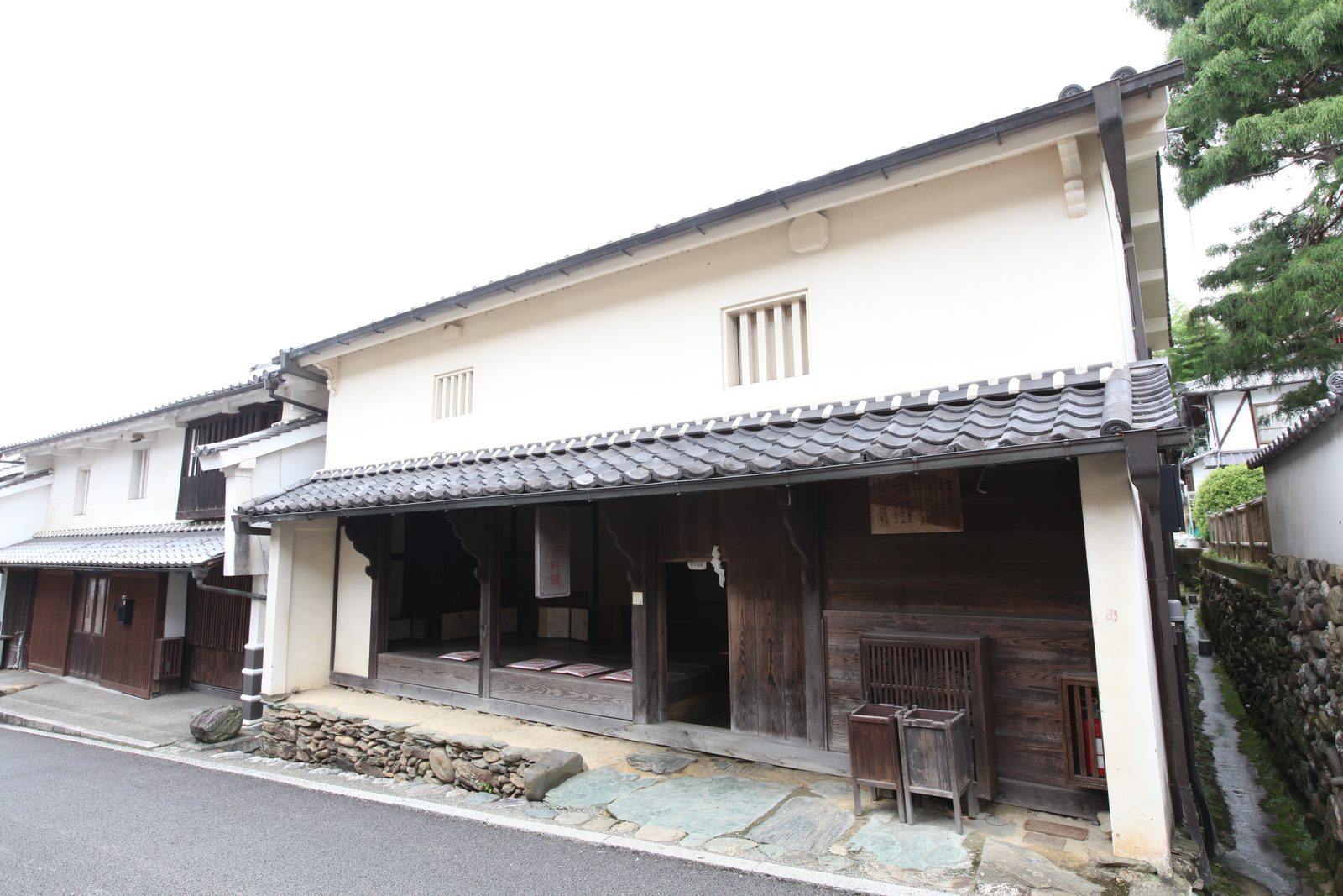 A white-walled storehouse-style building with a tiled eave and an open wooden front, beside a narrow stone-lined channel in the Yokaichi-Gokoku district