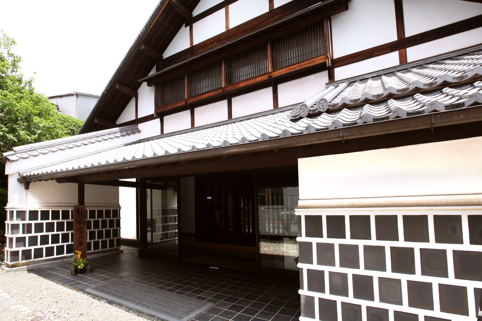 Entrance of the former wax-making residence building, with a tiled roof, white plaster walls and black-and-white checkered lower walls