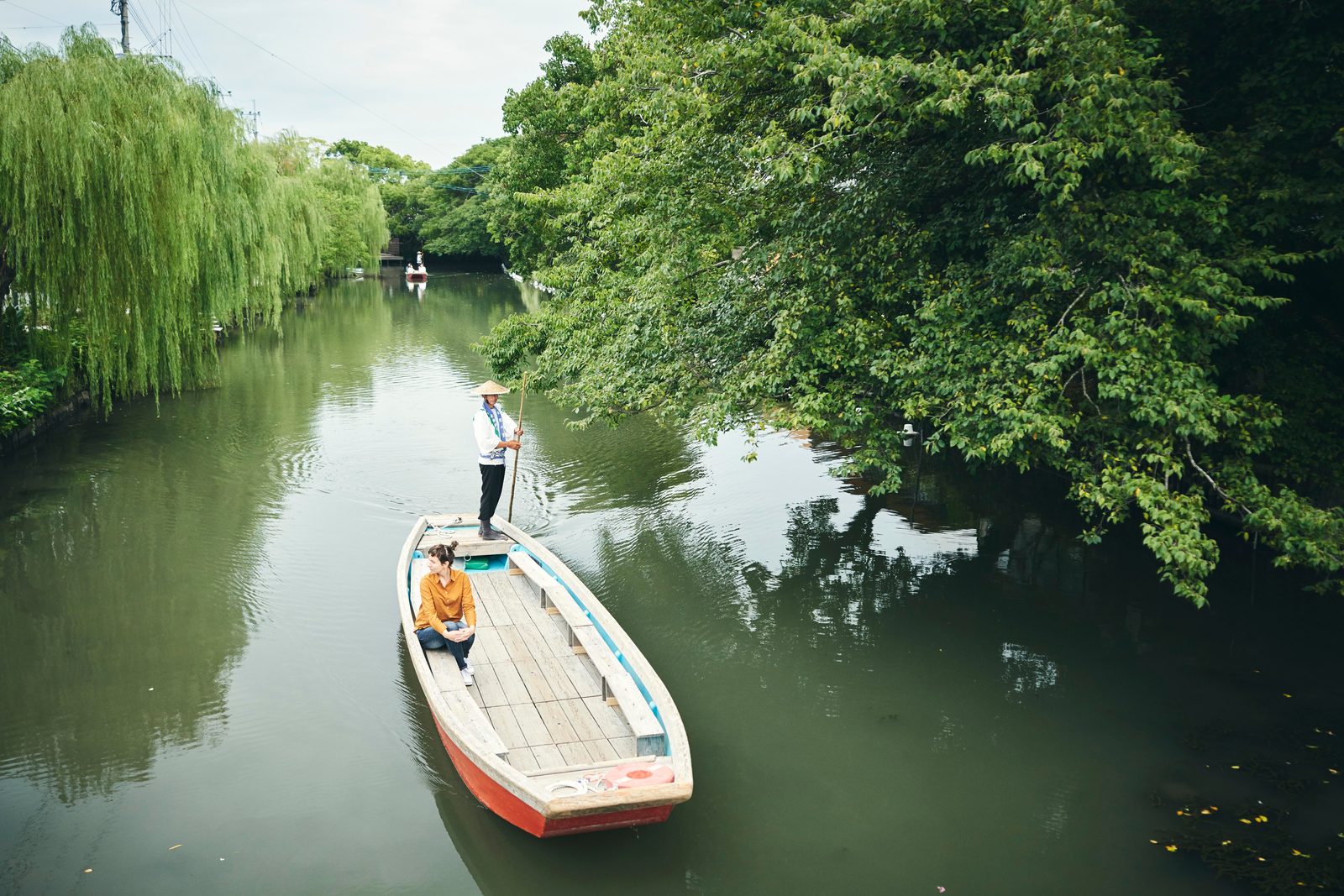 A boatman poles a river cruise boat beneath a willow tree in Yanagawa