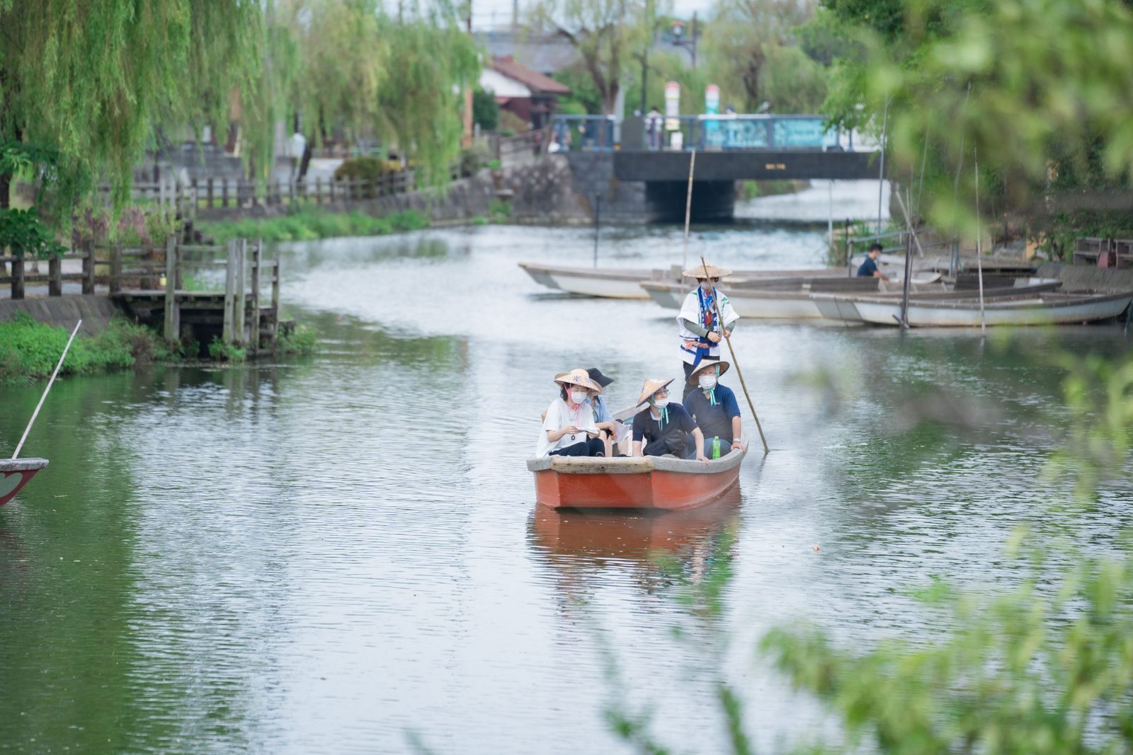 A boat carrying passengers in traditional hats along a willow-lined canal in Yanagawa