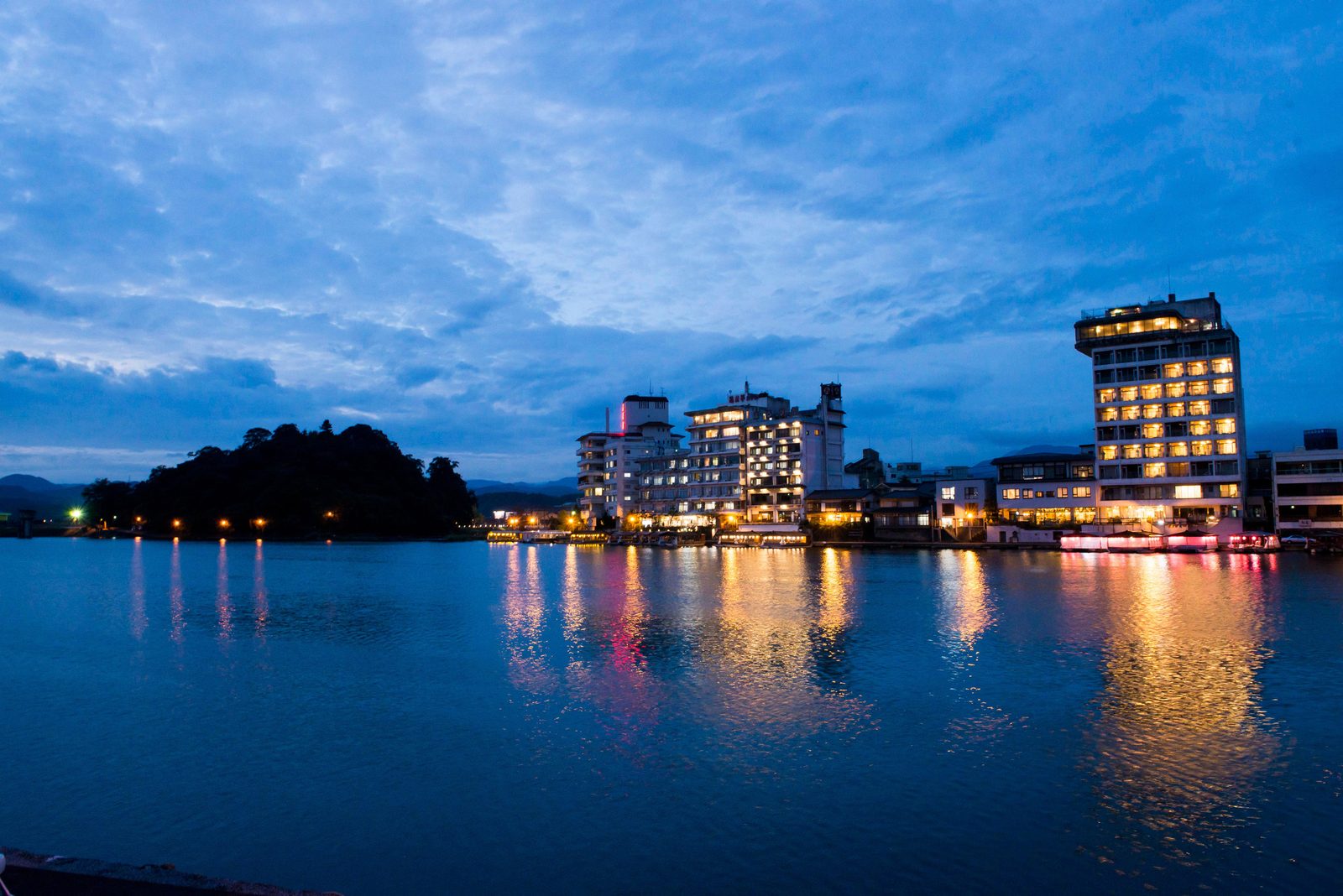 Riverside hotels lit at dusk beside the Mikuma River in Hita with a blue evening sky reflected on the water