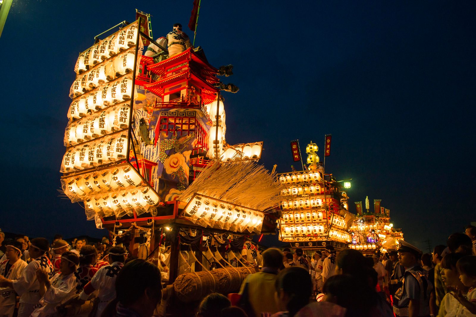 Tall lantern-hung festival floats lit at night among a crowd during the Hita Gion festival