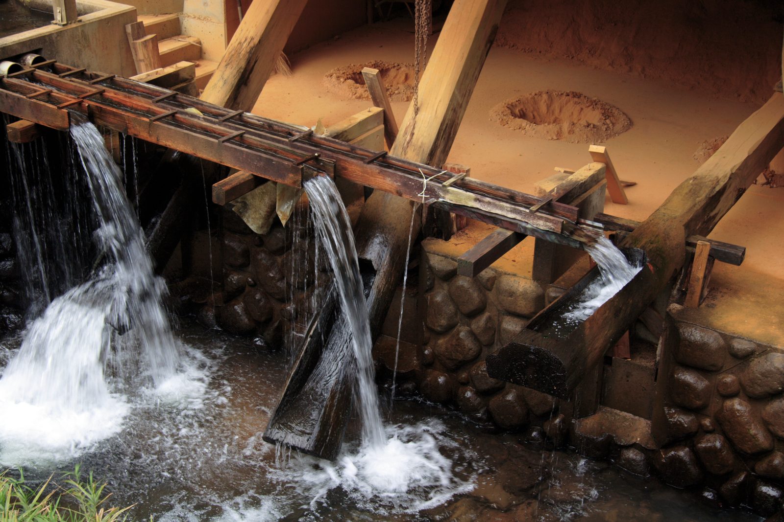 Wooden water-powered pounding beams with streams of falling water beside a stone wall at Onta pottery village near Hita