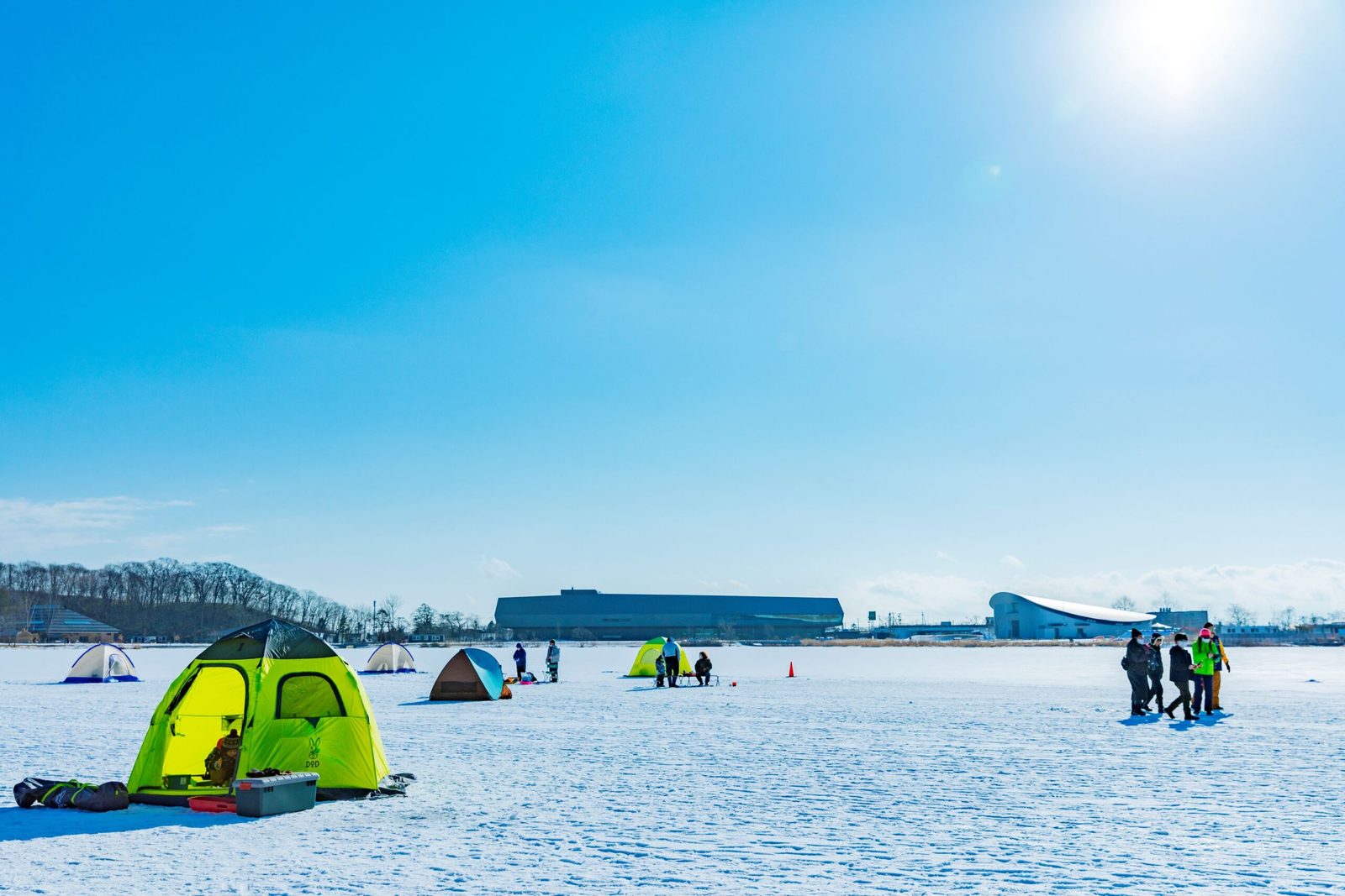 Ice-fishing tents on frozen Lake Poroto in winter, with the Upopoy buildings on the far shore