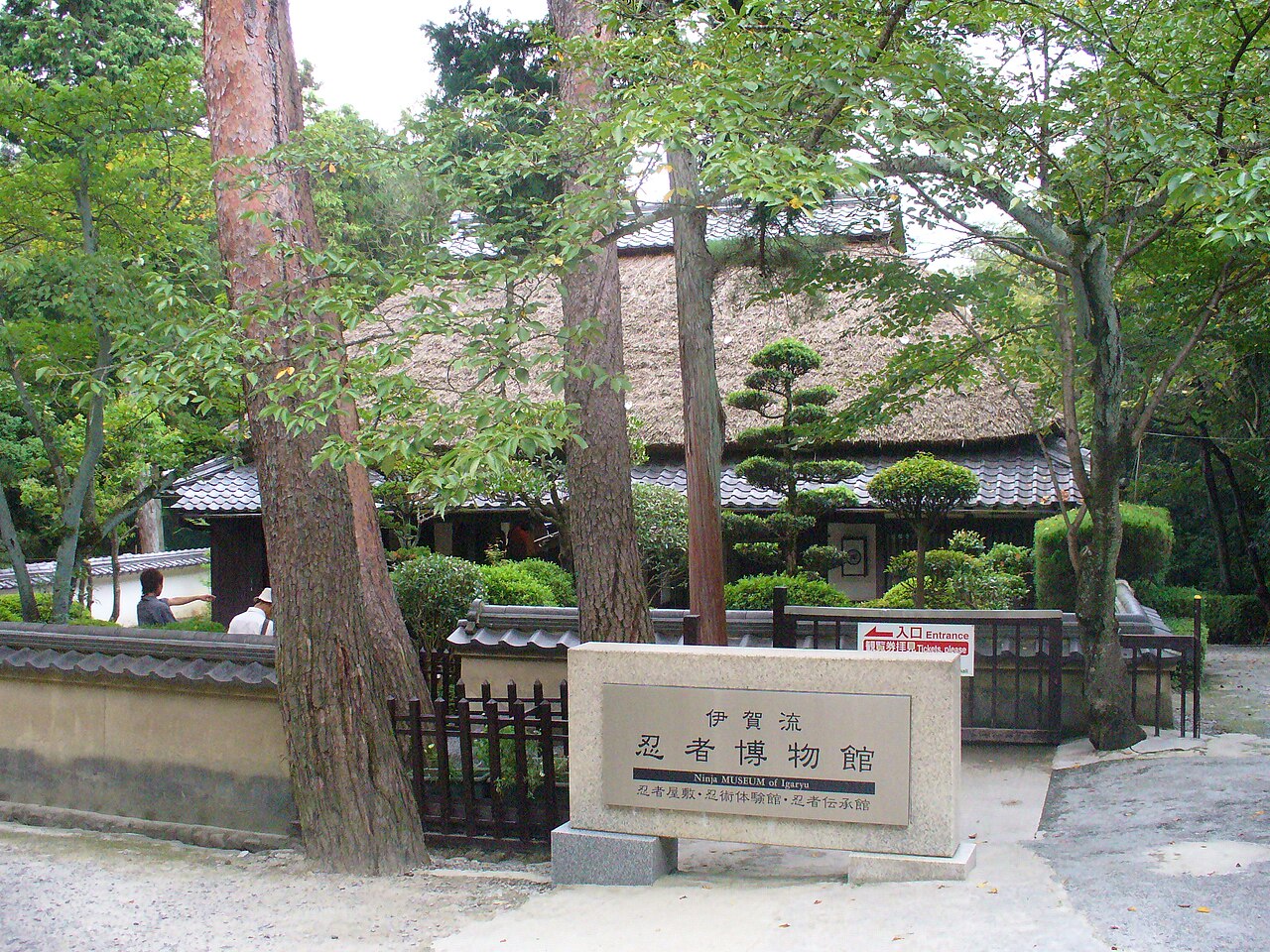 The entrance of the Iga-ryu Ninja Museum, with a stone name plaque in front of a thatched-roof farmhouse among tall trees