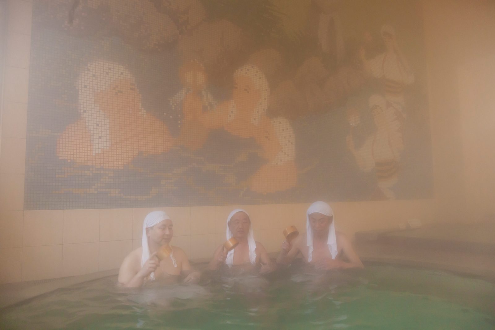 Bathers with white towels wrapped on their heads soak in a steaming indoor pool at Iwai Onsen, the yu-kamuri custom