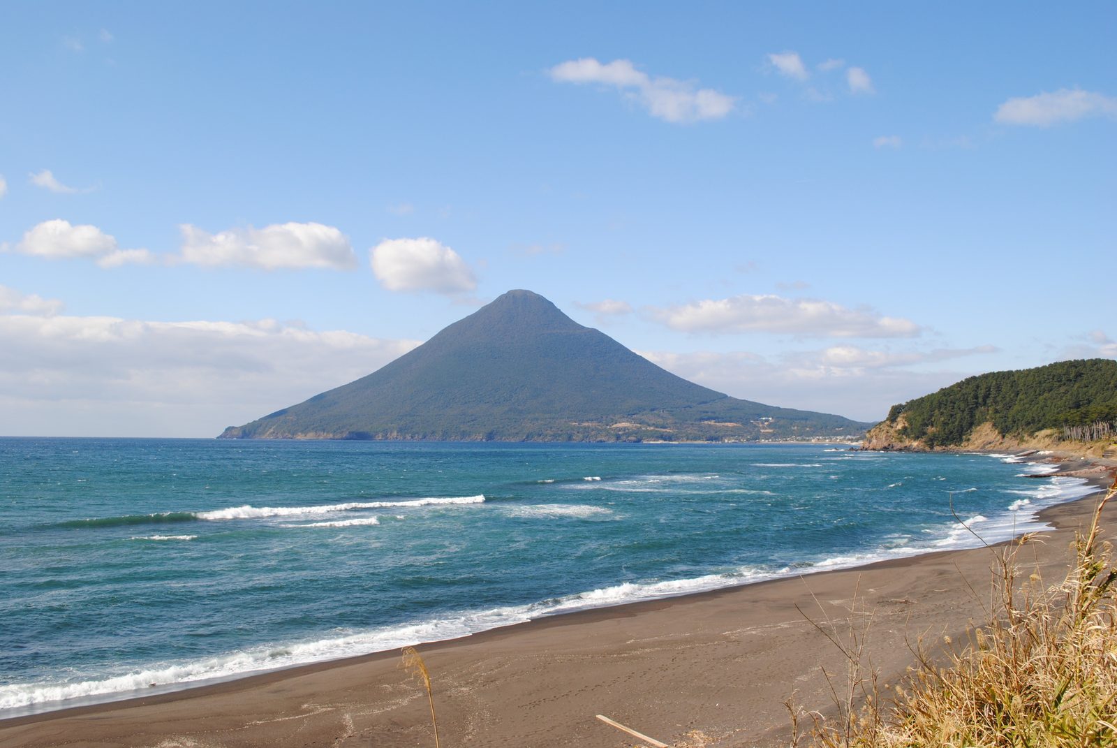 Kaimondake seen across blue sea and white surf from the beach near Nagasakibana, a green headland to the right