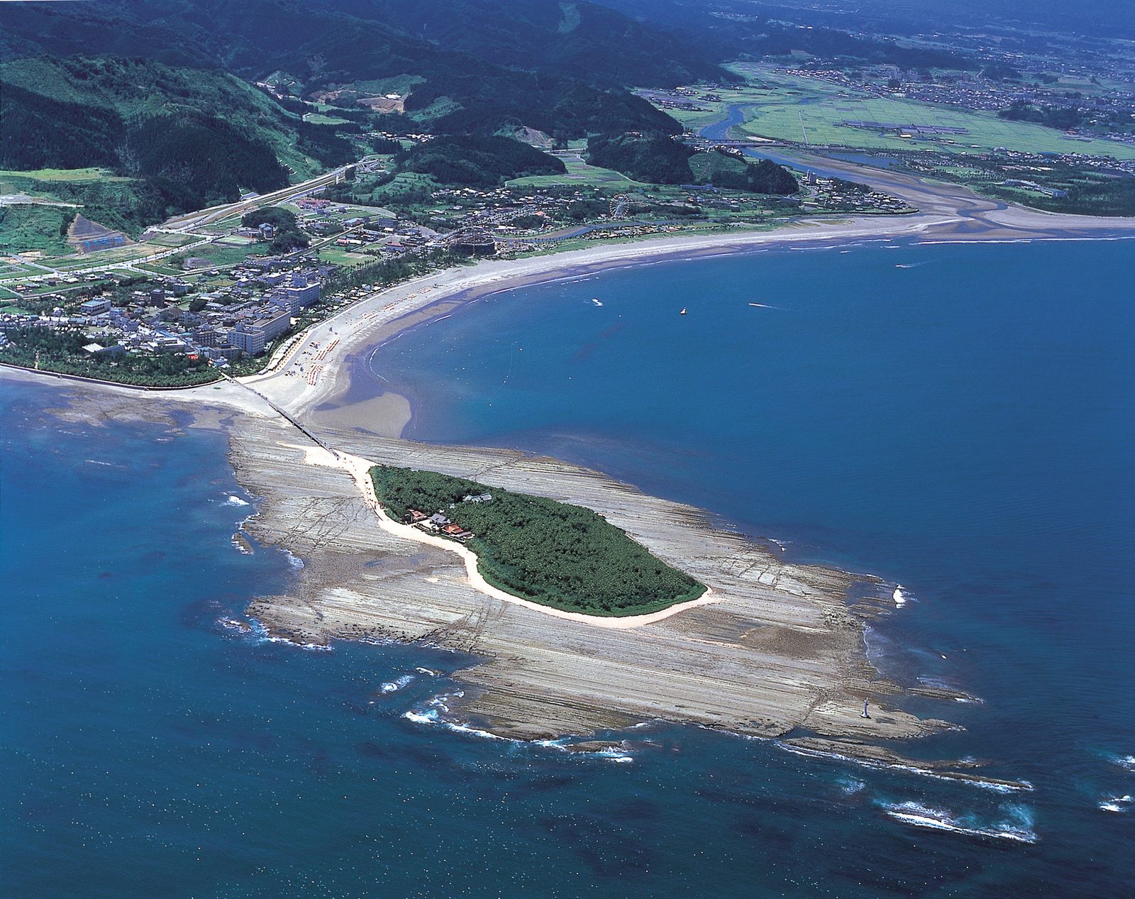 Aerial view of the small round island of Aoshima ringed by pale rock shelf, with the curving Miyazaki coast behind