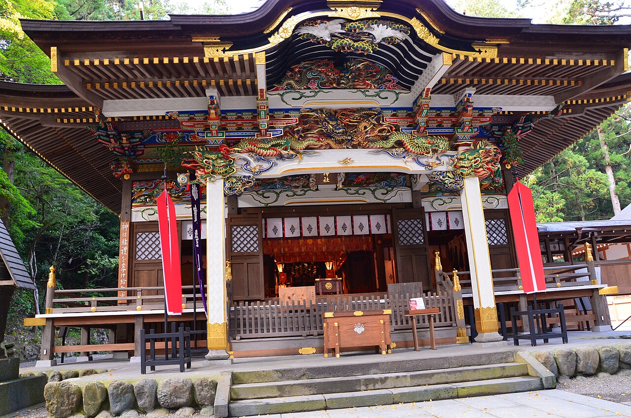 The ornately carved and painted front hall of Hodosan Shrine, with dragon carvings above the entrance and red ornamental flags on either side.