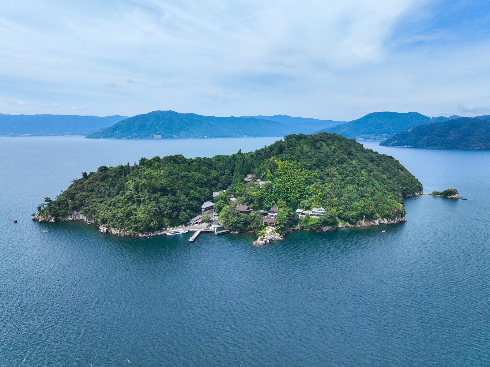 Aerial view of Chikubushima, with the pier and temple buildings on the shore and the lake and mountains behind
