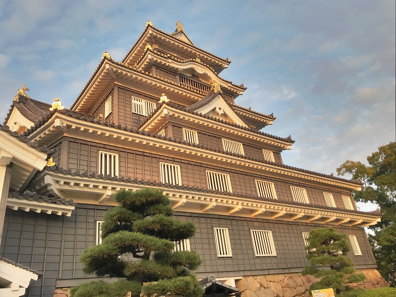 The black-lacquered keep of Okayama Castle rises above a pine, its white eaves catching low evening light against a pale sky.