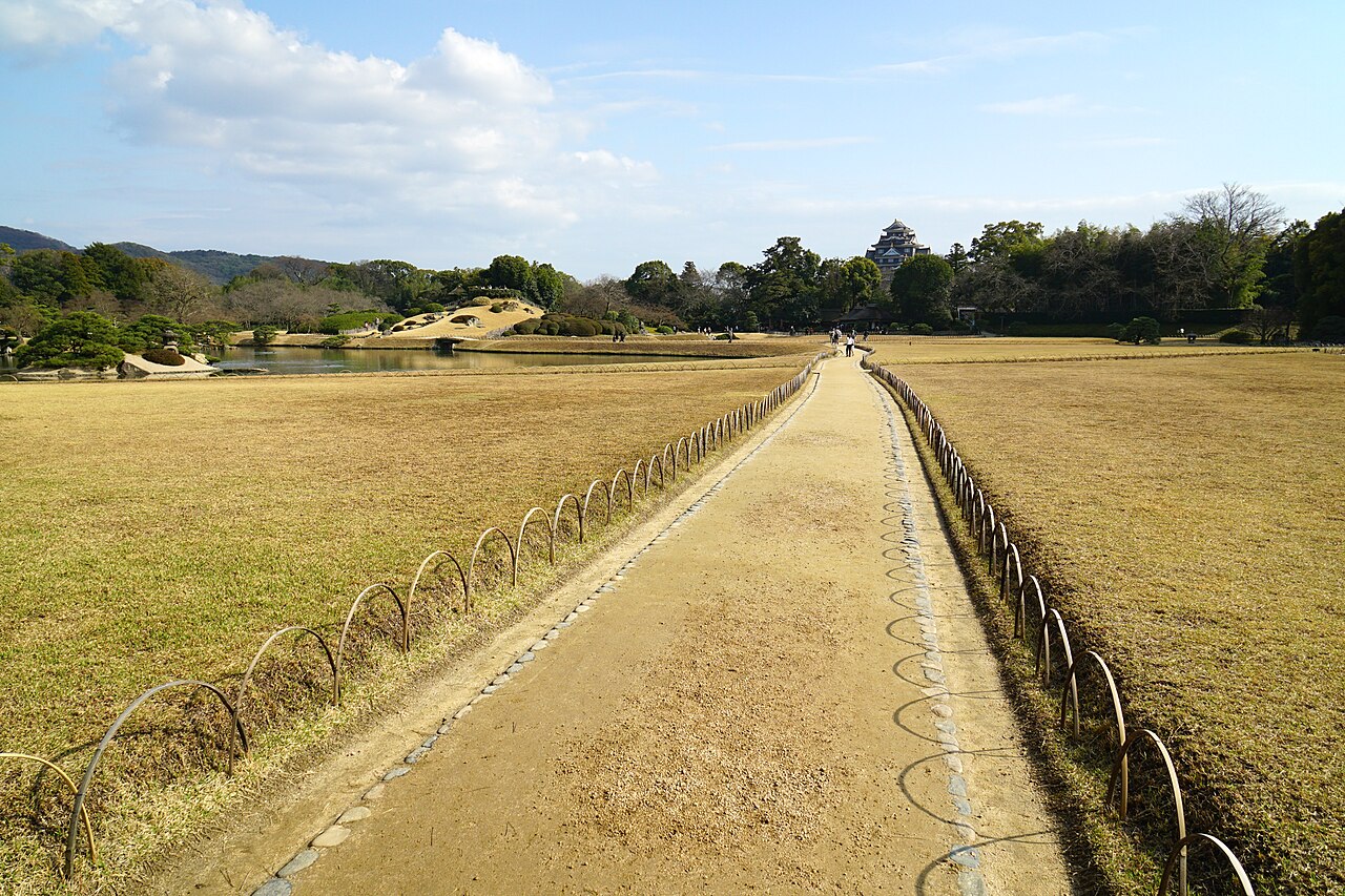 A wide gravel path crosses the dormant winter lawn of Korakuen, leading toward the distant keep of Okayama Castle with almost no one on it.