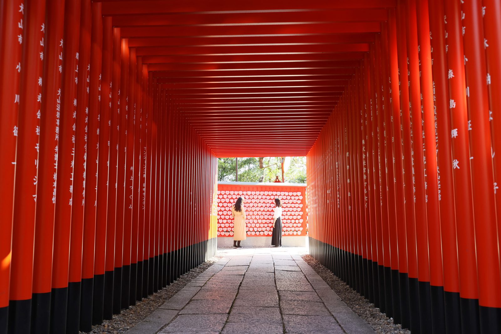 A tunnel of vermilion torii gates at Sanko Inari Shrine in Inuyama, with a wall of heart-shaped ema at the far end