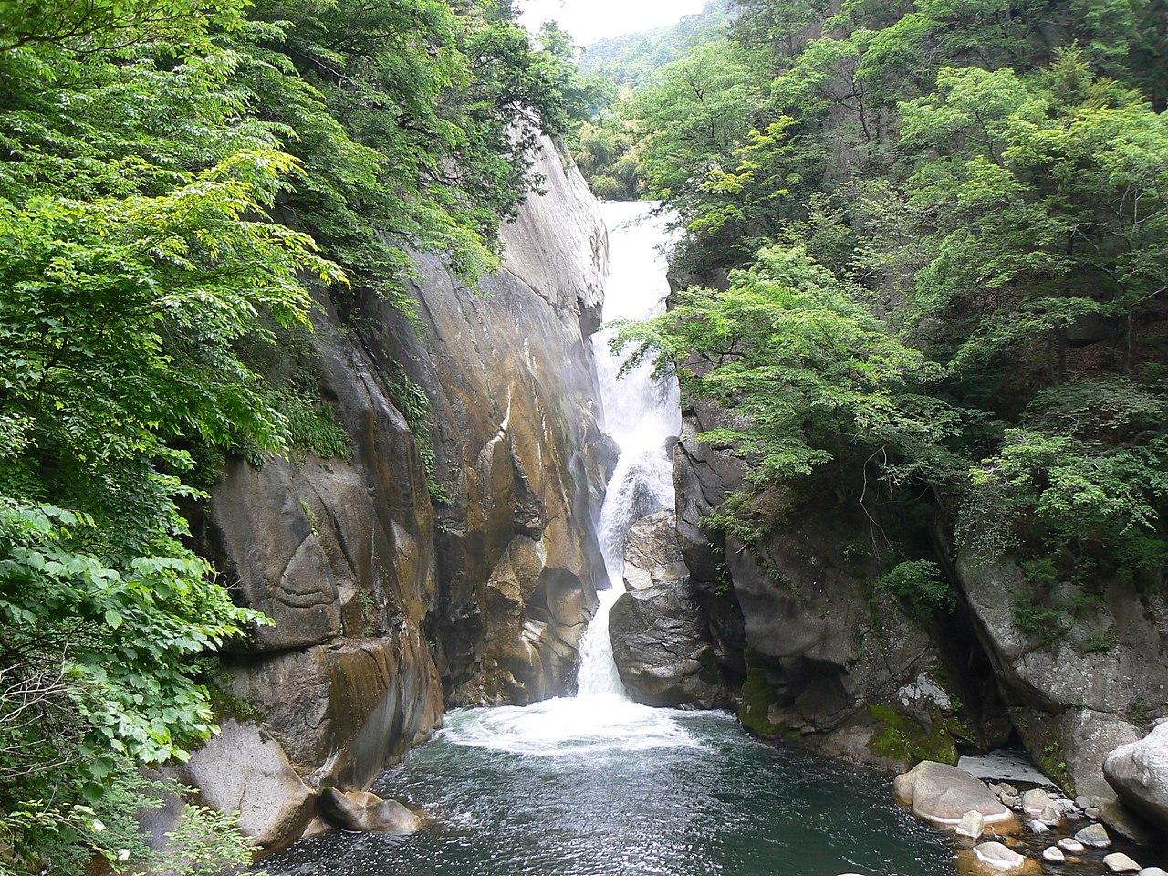 The Sengataki waterfall dropping into a green pool between wet rock walls.