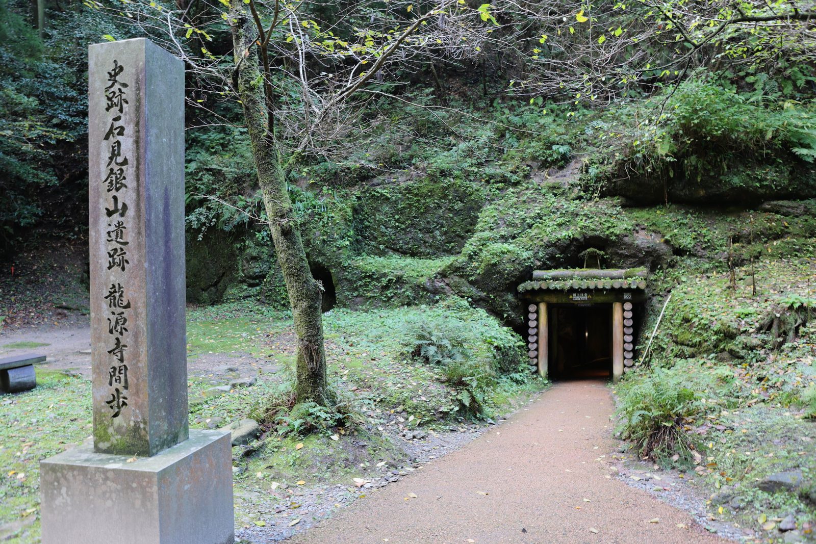 Stone marker beside a forest path leading to the dark mouth of the Ryugenji Mabu mine tunnel