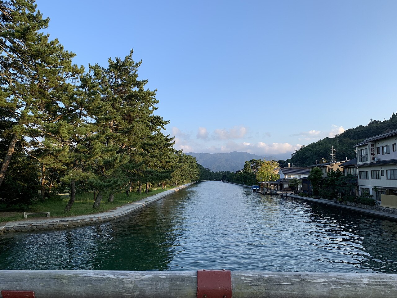 Calm canal lined with pine trees and townhouses in the Amanohashidate area of Miyazu on a clear day