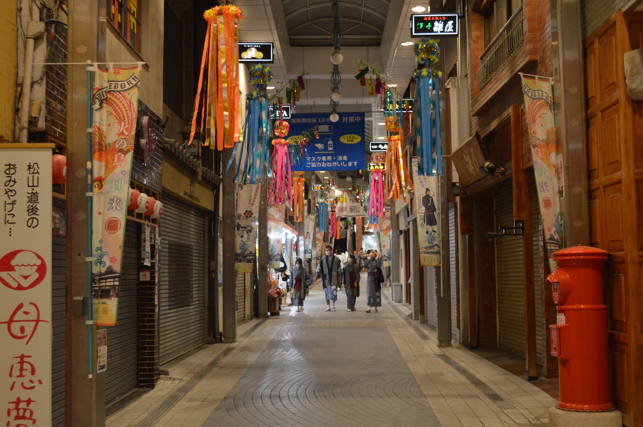 A covered shopping arcade hung with colorful lanterns and shop banners on Dogo Onsen's main street in Matsuyama.