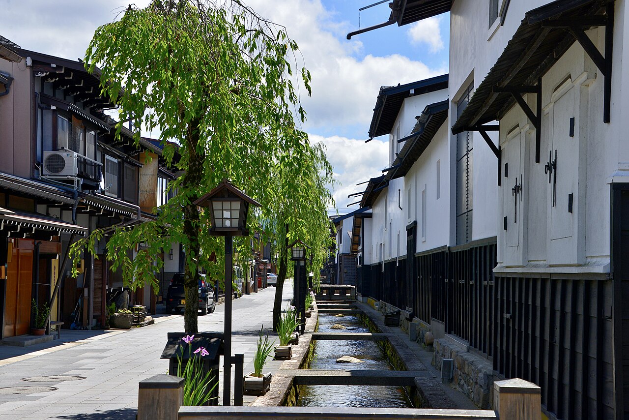 Willow trees and the stone-lined Setogawa canal beside white-walled storehouses on a sunny summer day in Hida Furukawa