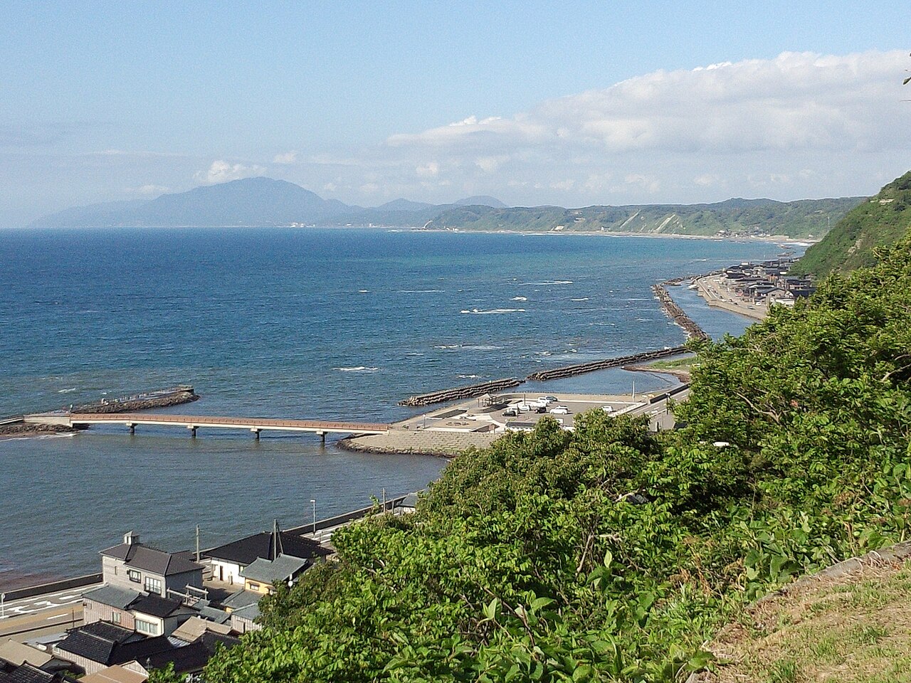 Izumozaki's row of townhouses along the shore seen from the hillside, with the harbour and the Sea of Japan beyond.