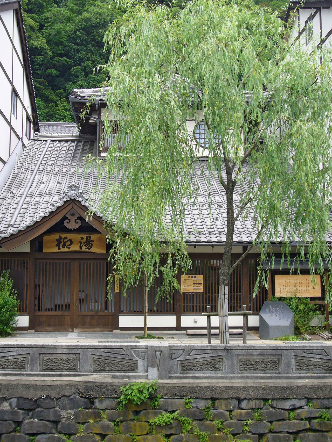 The Yanagi-yu communal bathhouse in Kinosaki Onsen, Toyooka, with a willow tree draping over its tiled roof.