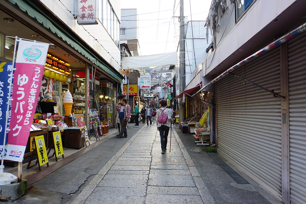The paved approach to Kotohira-gu, lined with shops selling udon and souvenirs, with a visitor walking uphill.