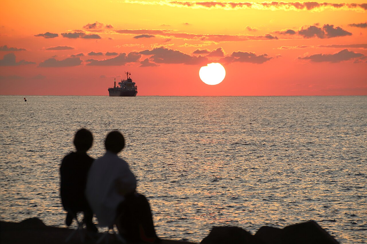 Two people sitting on the shore at Mikuni Beach, watching the sun set over the sea