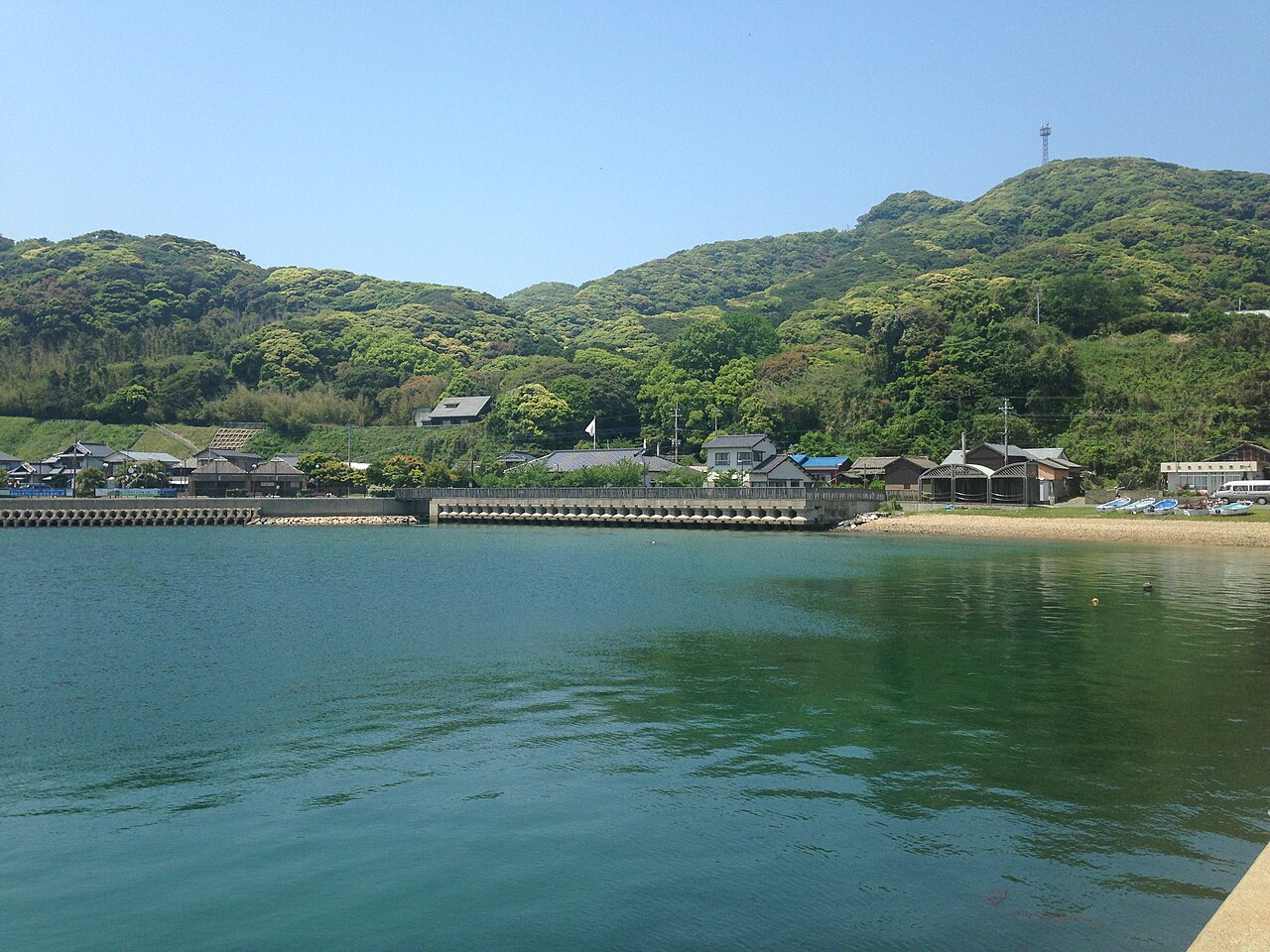 Calm green water of Oshima harbour with low houses and wooded hills behind