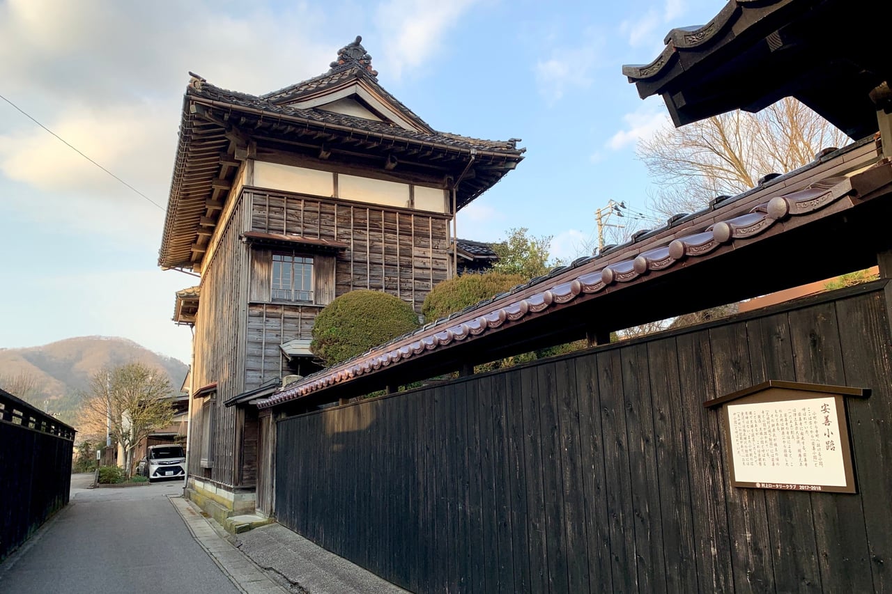 A quiet lane lined with black wooden fences and a traditional timber merchant house in the old castle town of Murakami.