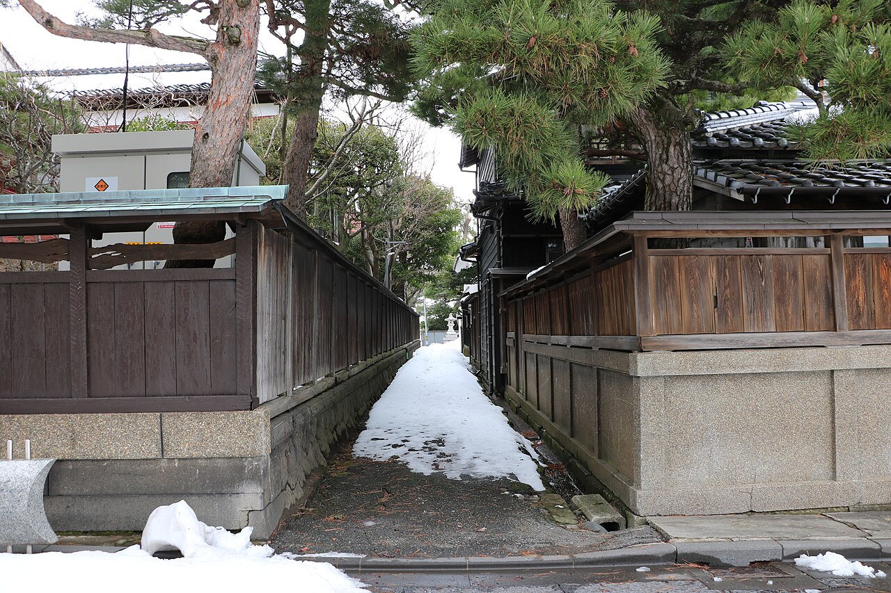 A narrow snow-covered lane between old wooden walls and pine trees in Sakata