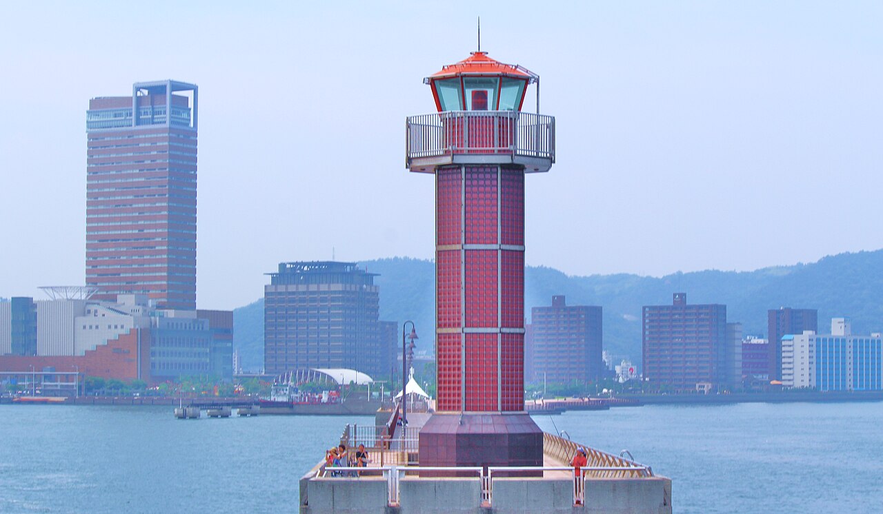 The red Tamamo breakwater lighthouse at the end of a pier, with the Takamatsu waterfront buildings and hills behind it