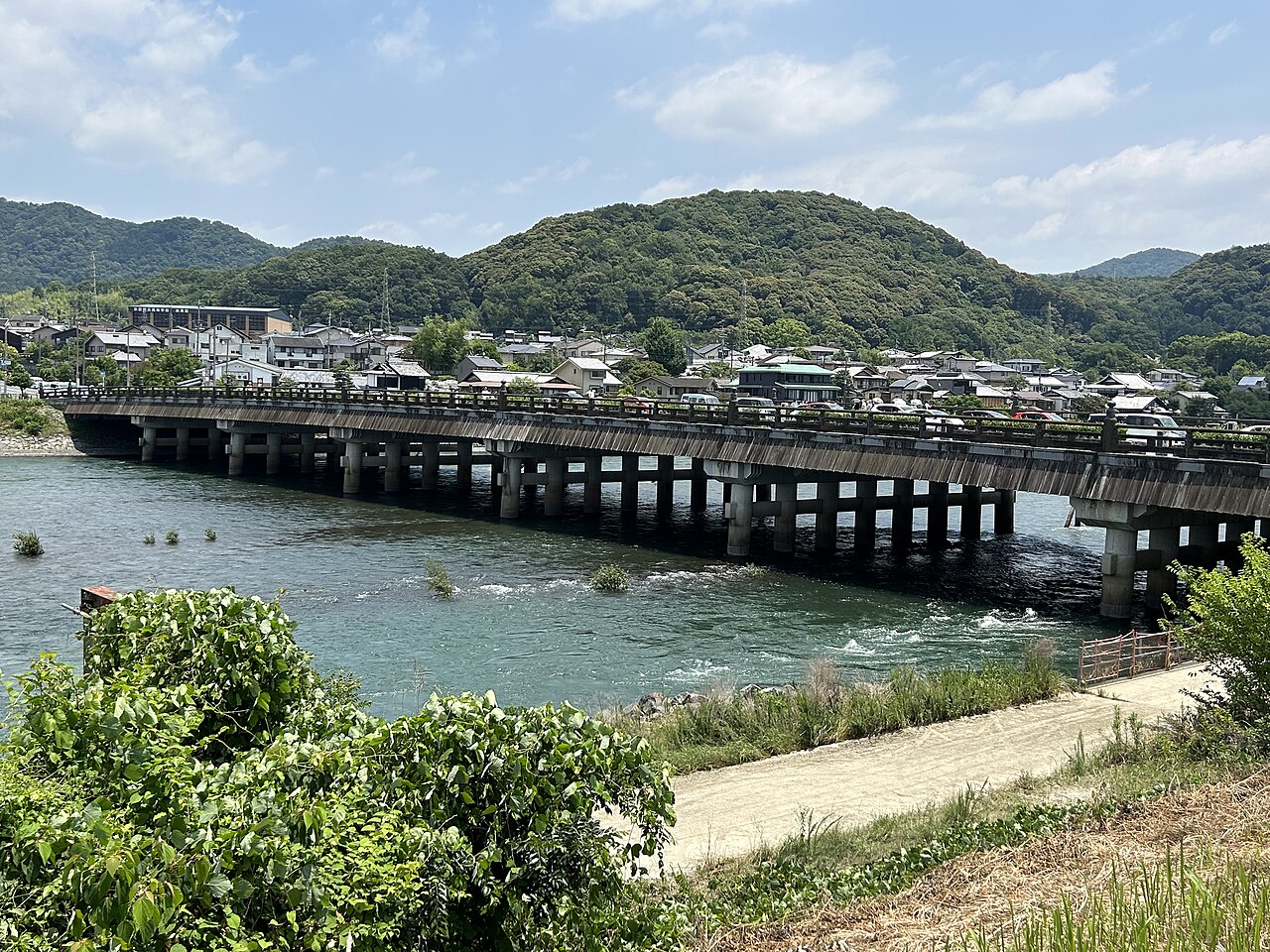 The Uji Bridge spanning the Uji River with a town and wooded hills in the distance, seen from the left bank