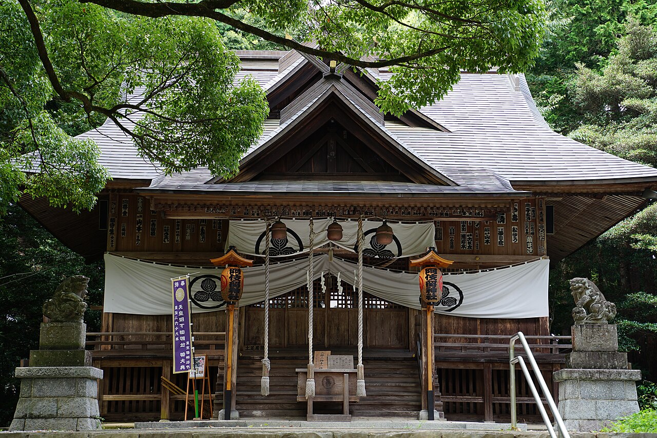 The worship hall of Akiru Shrine in Akiruno, its wide timber front hung with white curtains and flanked by a pair of stone guardian lions.