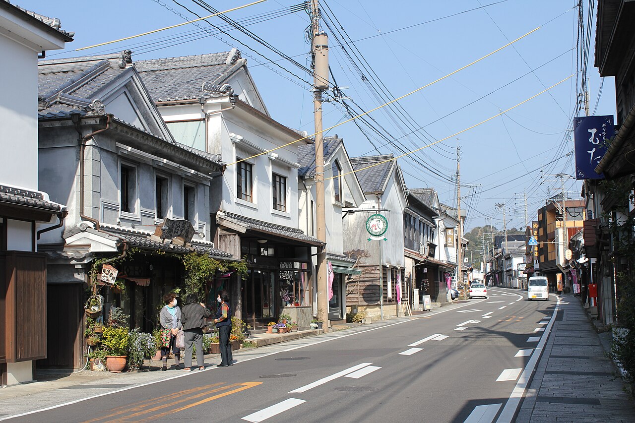 Tile-roofed merchant houses along a street in Arita's old town, with wooded hills rising behind