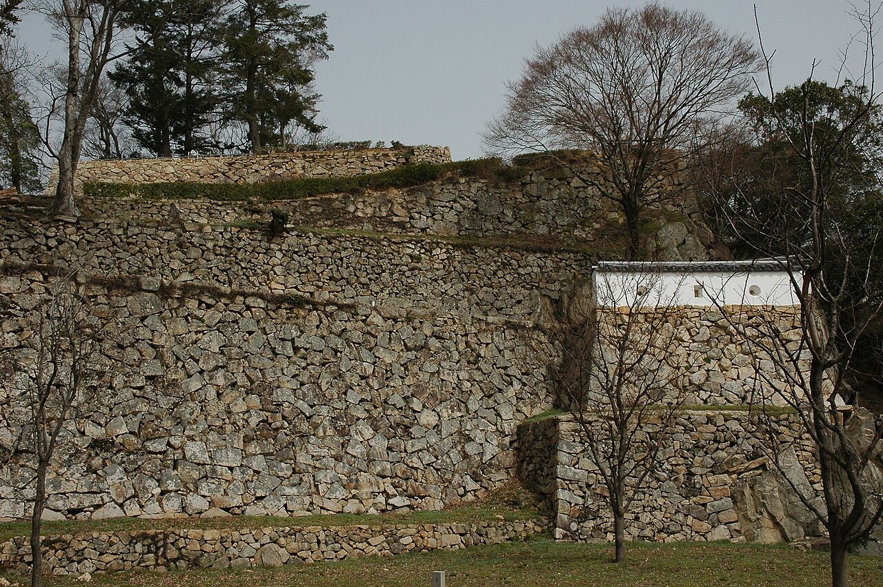 Tiered dry-stone walls of Bitchu Matsuyama Castle with a white plastered earthen wall on top, under bare winter trees