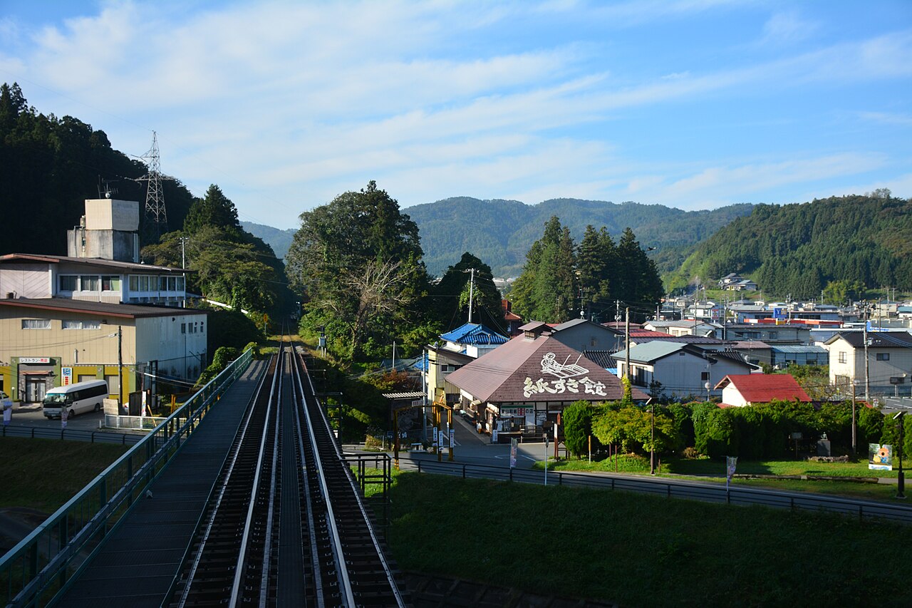 The end of the platform and single track at Geibikei Station, looking over the small town and forested hills of Higashiyama under a blue sky