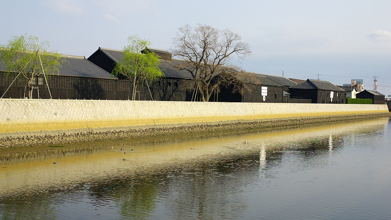A long row of black-boarded storehouses behind the canal wall in Handa