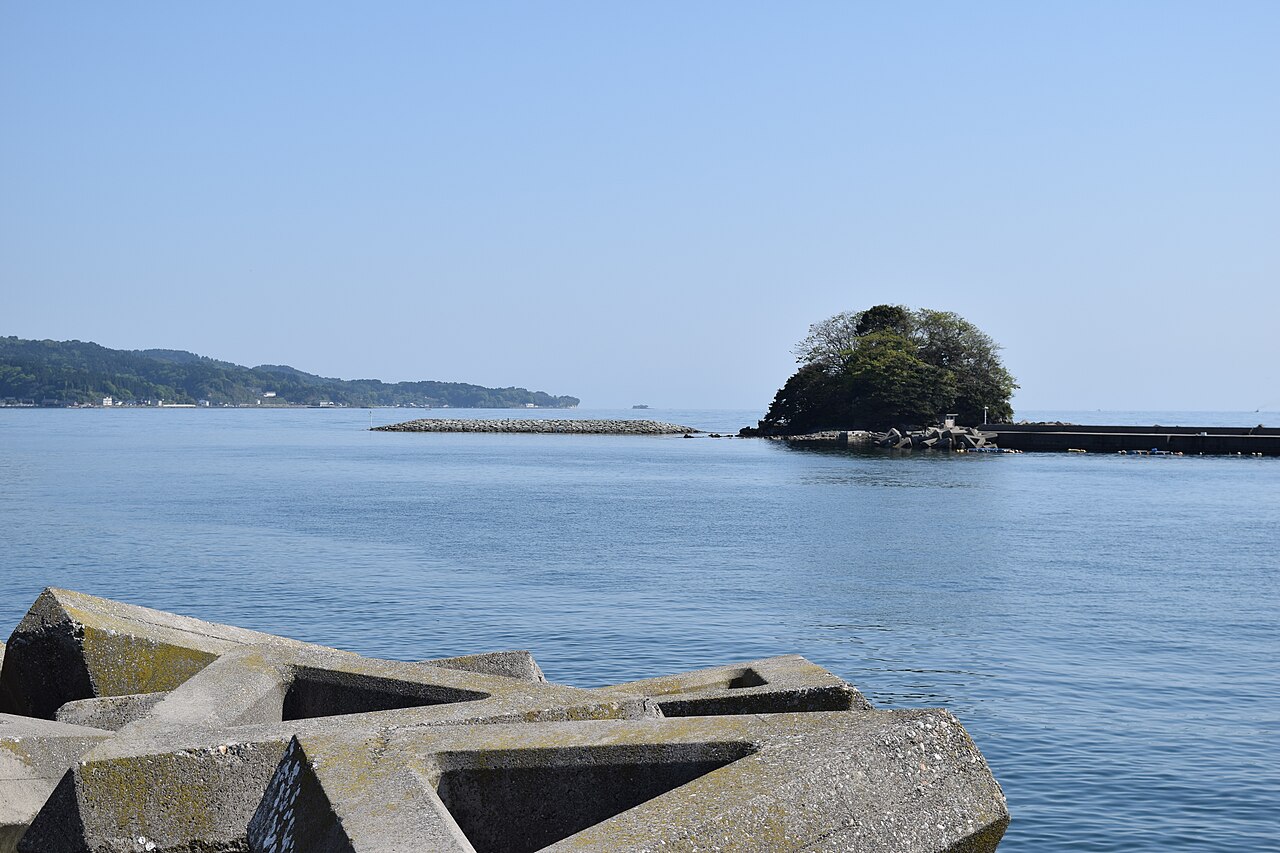 A small rocky island in blue water beyond a breakwater