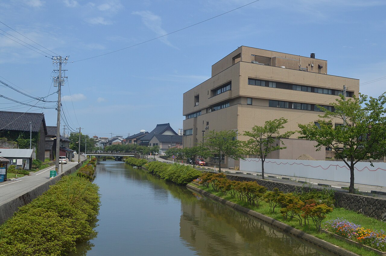 A narrow river with green banks and a museum building beyond