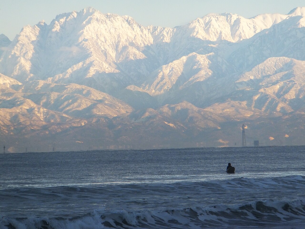 Snow-covered mountain range rising beyond the sea, seen from the Himi coast
