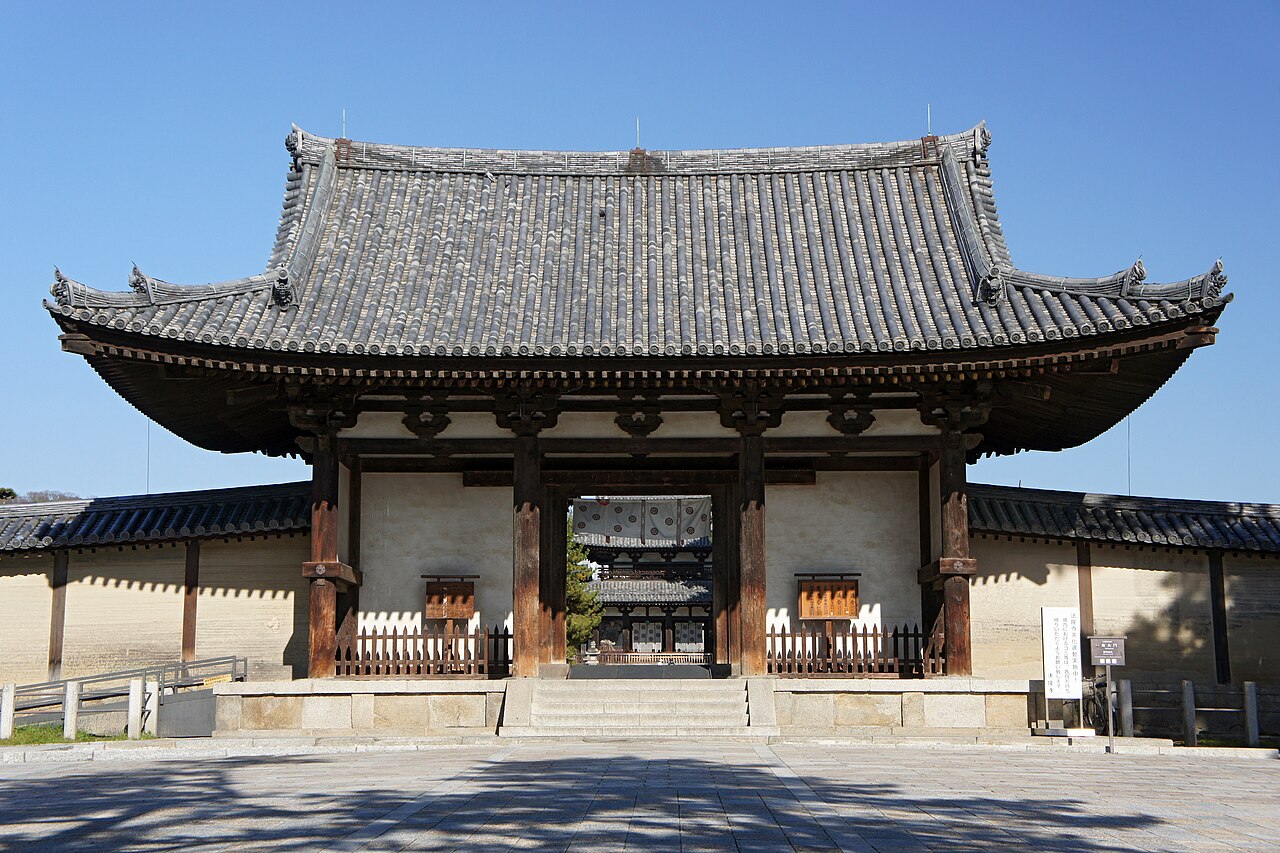 Horyuji's Chumon middle gate, a heavy tiled roof over dark wooden posts, set into the long white-walled corridor of the western precinct
