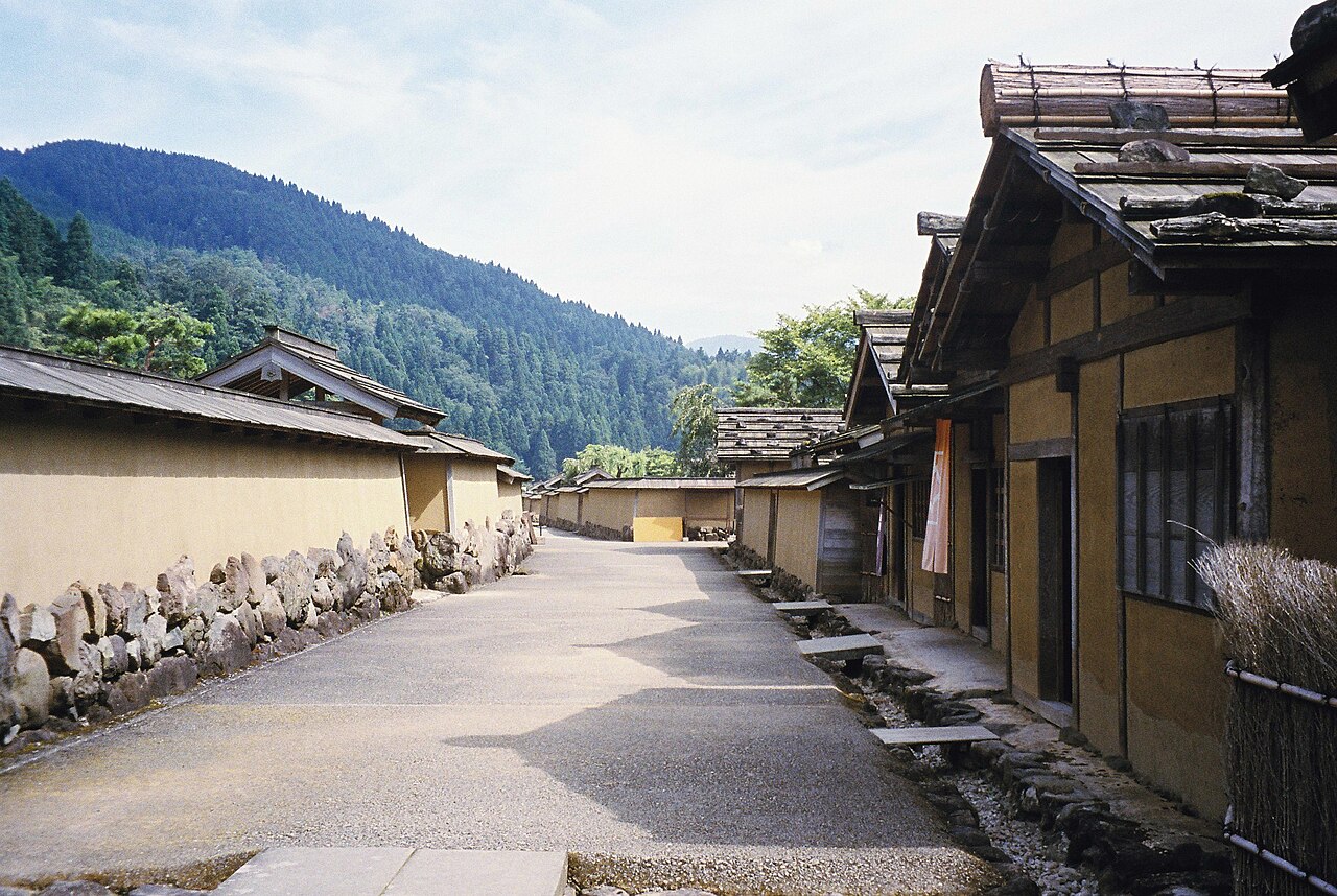 The rebuilt street of the Restored Townscape at Ichijodani, with earthen walls, low wooden houses, a stone-edged gutter and wooded hills behind