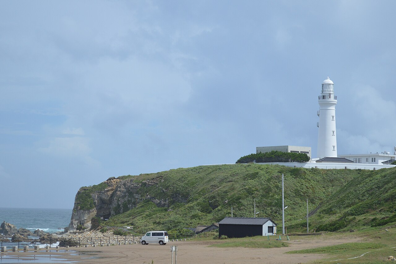 The white Inubosaki Lighthouse standing on a green headland above the rocky shore of Cape Inubo