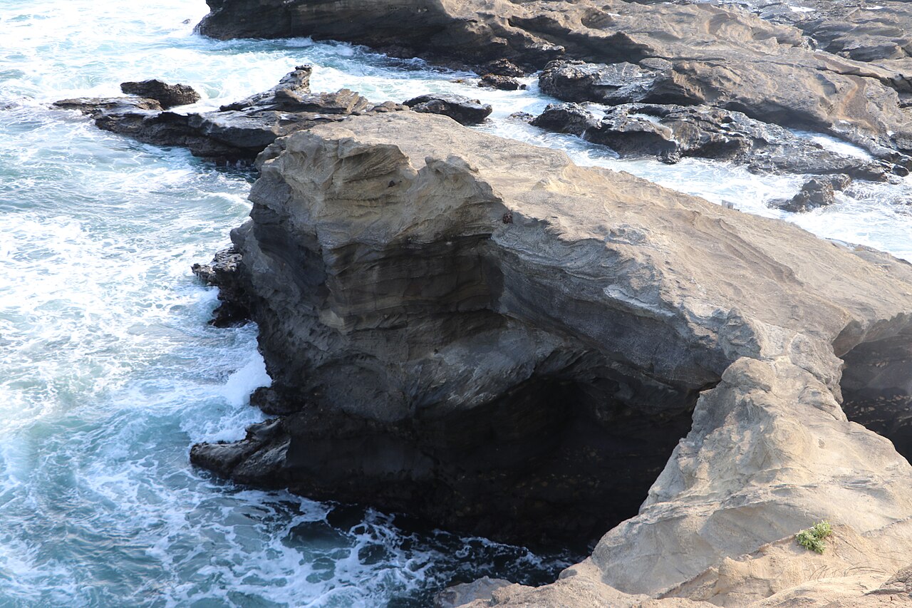 An aerial view of the pale sandstone Umanose rock arch on the Jogashima shore with waves washing over the rocks