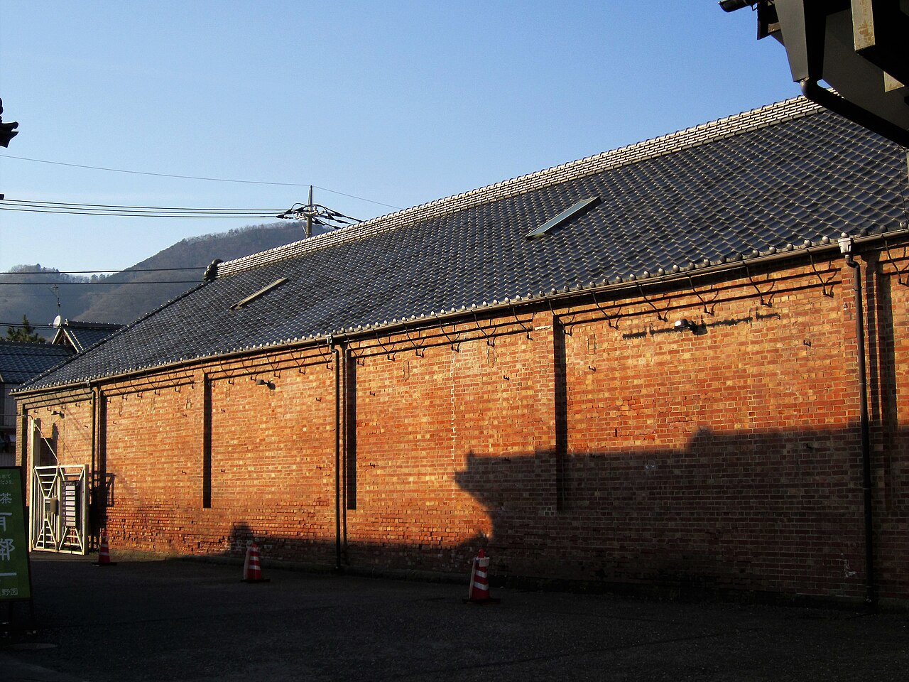 The long brick wall and tiled roof of a Yurinkan storehouse, lit orange by low afternoon sun.