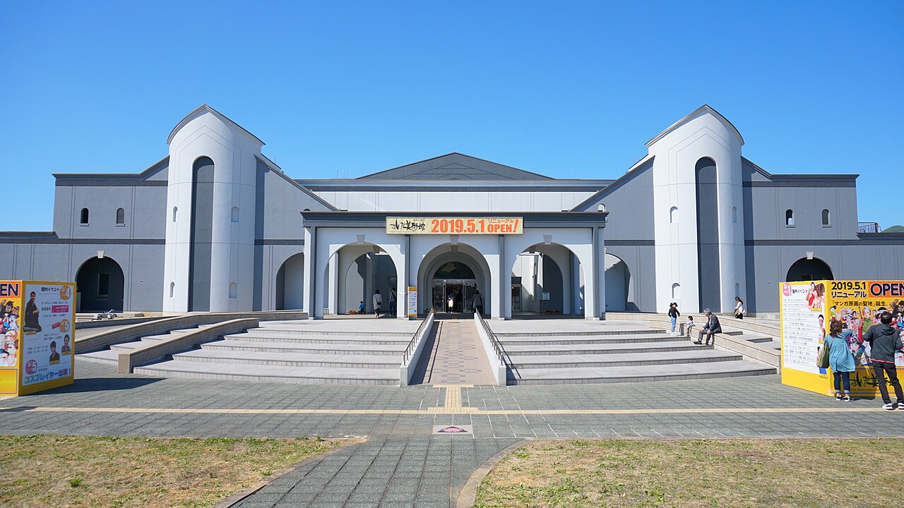 A broad cream-and-white museum building with tall arched towers and a wide stepped entrance, with visitors near the doors under a clear sky.