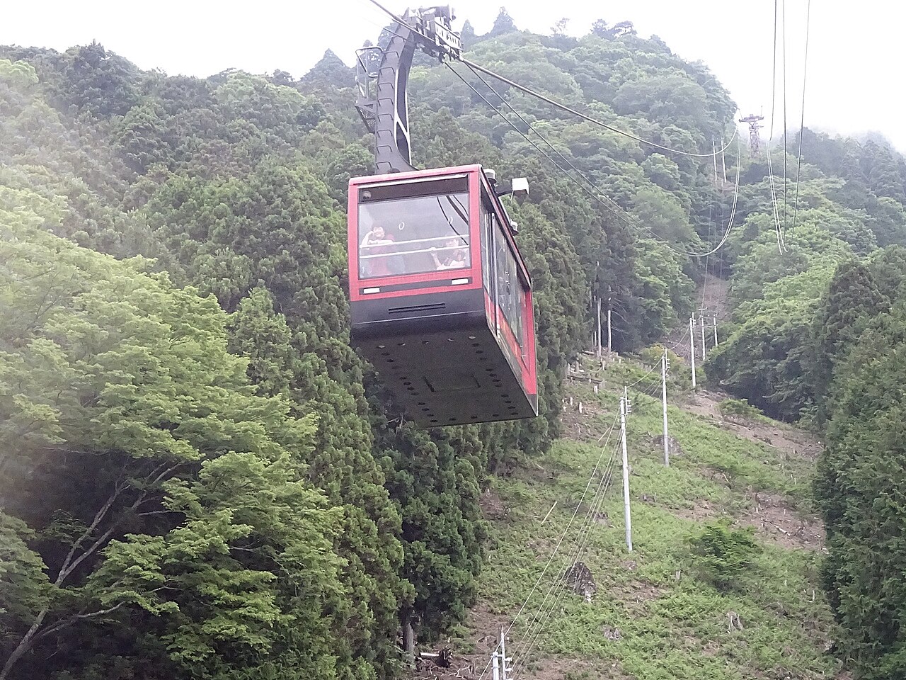 A red gondola of the Mt. Minobu ropeway climbing a forested slope