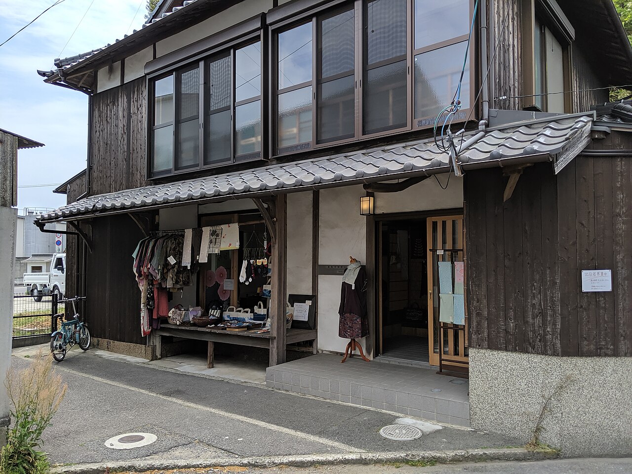 A weathered wooden two-storey shop with a tiled awning facing a quiet street in the Honmura district of Naoshima