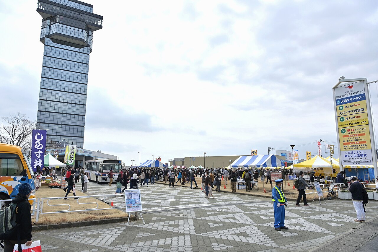 The tall glass Oarai Marine Tower rising above an event plaza with crowds, tents and banners on a spring day