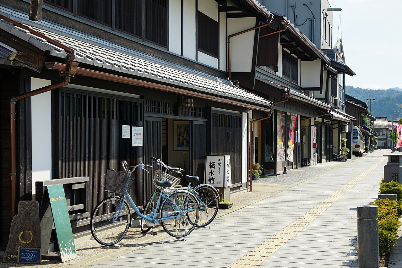 Wide paved street in Obama Nishigumi lined with tiled-roof townhouses, with a bicycle at the entrance of a townhouse gallery